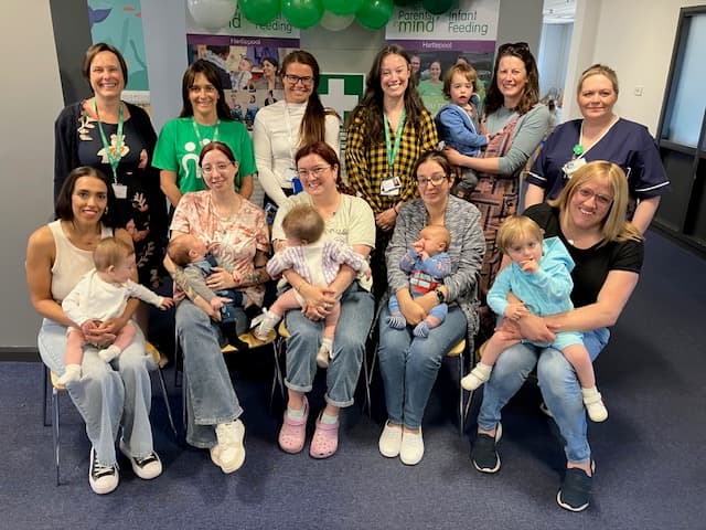 New Parents, babies, Hartlepool staff and staff from other organisations smiling at the camera at Hartlepool's first Birthday celebration. Behind them are NCT banners and balloons